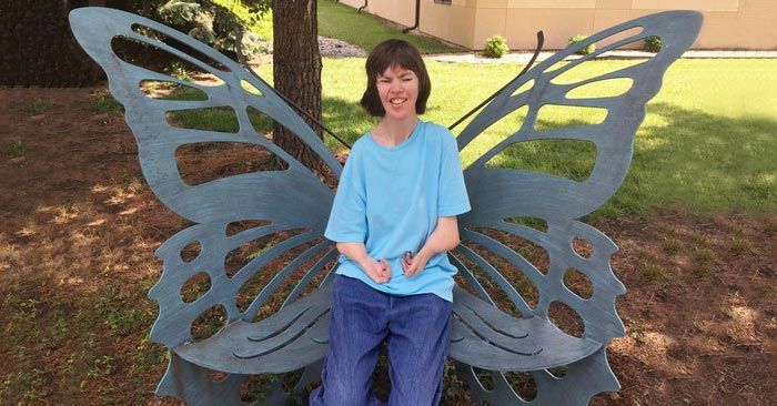 Heather Madsen, woman with disabilities sitting on a metal butterfly chair in a park.